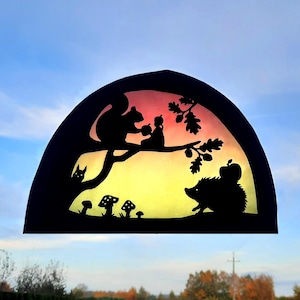 Può includere: Una silhouette nera di uno scoiattolo, un riccio e una piccola figura che tiene una mela su un ramo d'albero su uno sfondo sfumato di tramonto. La scena è incorniciata da un semicerchio nero con alcuni funghi in basso.
