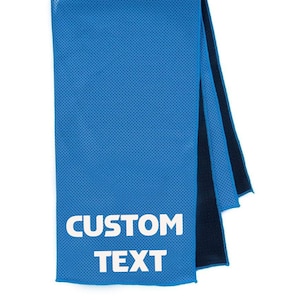 May include: A blue cooling towel with the words "CUSTOM TEXT" in white block letters. The towel is folded in thirds, revealing a dark blue backing. The towel has a perforated texture.