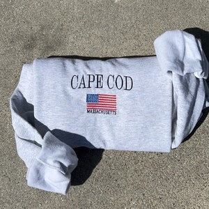 May include: Gray sweatshirt with the text "CAPE COD" and an embroidered American flag with the text "MASSACHUSETTS" underneath.