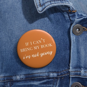 Puede incluir: Botón naranja con texto blanco que dice "Si no puedo traer mi libro, no voy". El botón está sujeto a una chaqueta vaquera azul.