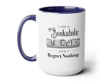 Puede incluir: Taza de café de cerámica blanca con borde azul. La taza tiene un gráfico negro que dice "Soy un adicto a los libros y no me arrepiento de nada" con una pila de libros en un estante.