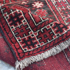 May include: A red and black patterned rug with a fringed border. The rug features a geometric design with intricate details.