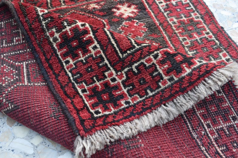 May include: A red and black patterned rug with a fringed border. The rug features a geometric design with intricate details.