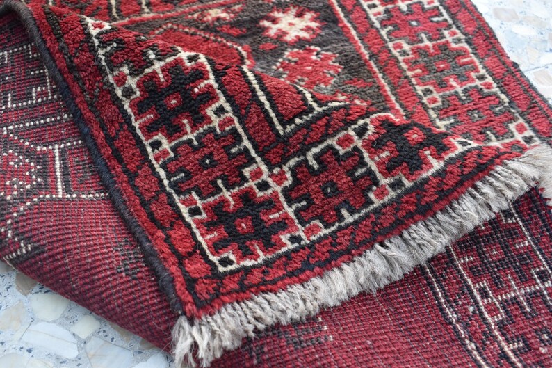 May include: A red and black patterned rug with a fringed border. The rug features a geometric design with intricate details.