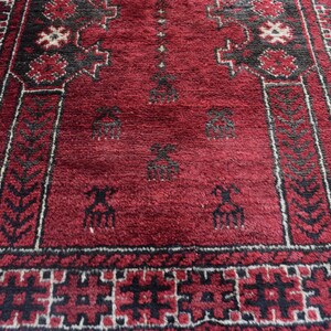 May include: A red prayer rug with black and white geometric patterns. The rug features a traditional design with intricate details.