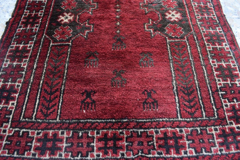 May include: A red prayer rug with black and white geometric patterns. The rug features a traditional design with intricate details.