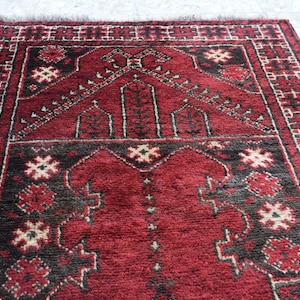 May include: A red prayer rug with a black and white geometric pattern. The rug has a traditional design with a central medallion and borders.