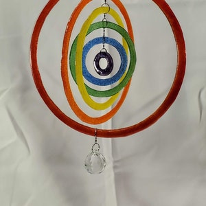 May include: A colorful, hanging mobile featuring concentric, oval-shaped rings in a rainbow of colors: red, orange, yellow, green, blue, and purple. A clear crystal ball hangs from the bottom. The mobile is suspended by a thin metal chain.