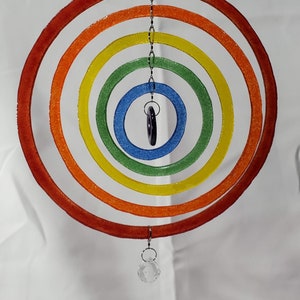 May include: A colorful, hanging mobile featuring concentric circles in a rainbow of colors: red, orange, yellow, green, and blue. A dark purple pendant and a clear crystal ball dangle from the center. The mobile is suspended by a chain.