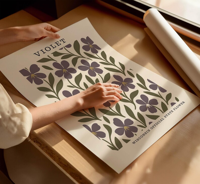 A person's hands are holding a poster with a floral design featuring purple flowers and green leaves.