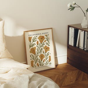 a framed poster of California poppies on a bedside table, with a bookshelf and a vase of white flowers in the background.