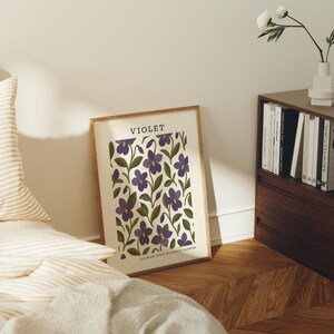 a bedroom scene with a framed poster of purple flowers on the wall, a bed with striped pillows, a wooden nightstand with a vase of white flowers, and a bookshelf filled with books.