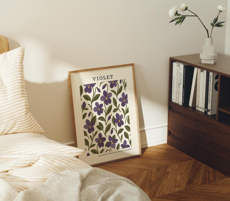 a bedroom scene with a framed poster of purple flowers on the wall, a bed with striped pillows, a wooden nightstand with a vase of white flowers, and a bookshelf filled with books.