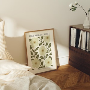 a framed poster of a flower design on a wall, with a bookshelf and a bed in the background.