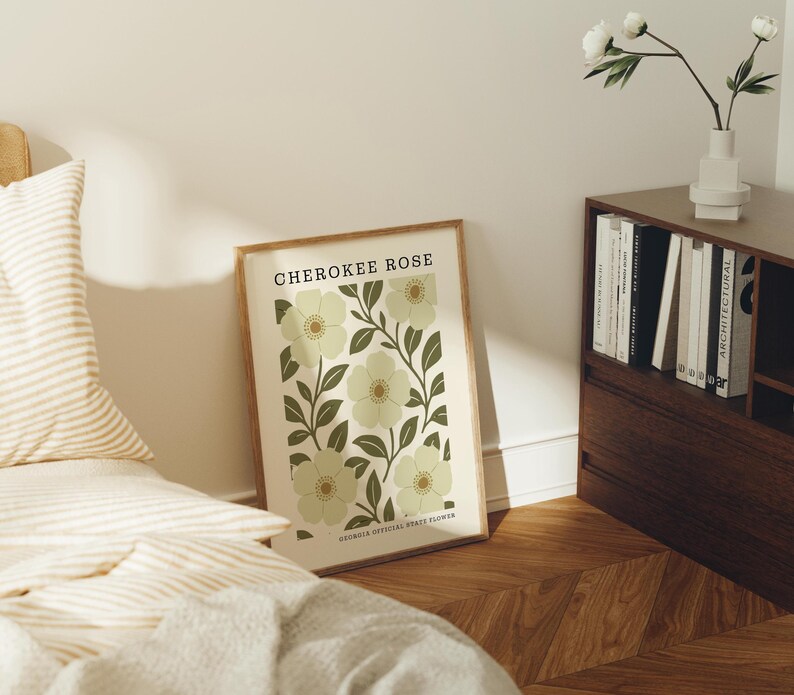 a framed poster of a flower design on a wall, with a bookshelf and a bed in the background.