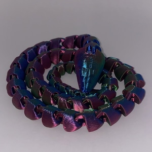 Puede incluir: Una cadena de plástico iridiscente multicolor. La cadena está enrollada en un círculo con un extremo puntiagudo que sobresale.