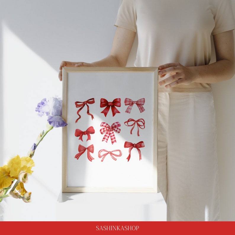 May include: A framed print with a white background and 12 red watercolor bows of various styles. The print is in a wooden frame and is sitting on a white surface.