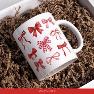 May include: White ceramic mug with a red and white bow pattern. The mug has a handle and is filled with brown packing peanuts.