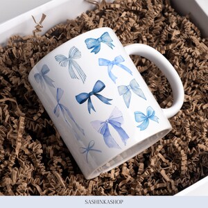 Pode incluir: Caneca de cer&acirc;mica branca com um padr&atilde;o de la&ccedil;o azul em aquarela. A caneca tem uma al&ccedil;a e est&aacute; sentada em uma trituradora de papel marrom.