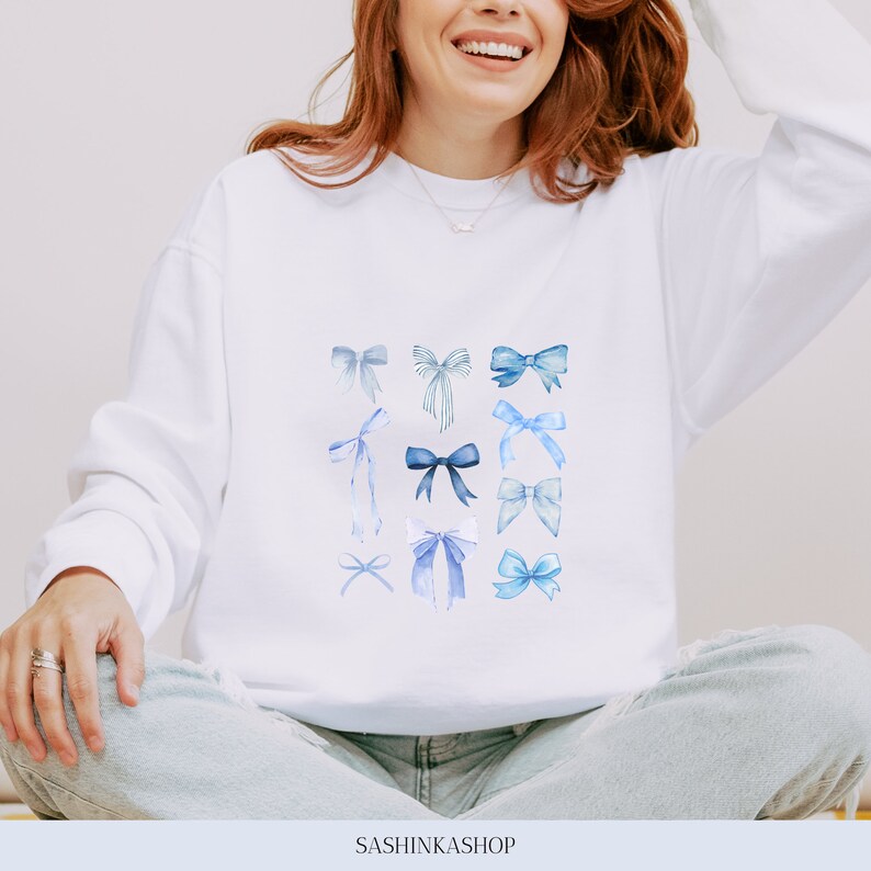 Pode incluir: Camisola branca com um padr&atilde;o de la&ccedil;os azuis em aquarela. O texto "SASHINKASHOP" est&aacute; impresso na parte inferior da camisola.