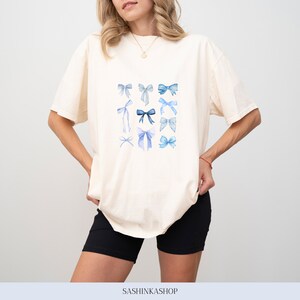 Pode incluir: Uma camiseta branca com um gr&aacute;fico de la&ccedil;os azuis de aquarela. Os la&ccedil;os est&atilde;o dispostos em um padr&atilde;o de grade.