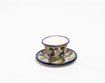 May include: A ceramic teacup and saucer set. The cup and saucer feature a colourful floral pattern in green, red, and yellow on a white background. The rims are trimmed with blue and yellow.