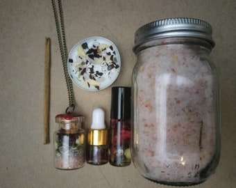 May include: A set of bath and body products including a jar of bath salts, a small bottle of essential oil, a small bottle of bath salts, a small candle, and a necklace with a charm.