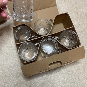 May include: A set of six clear glass mugs with a textured design, packaged in a brown cardboard box.