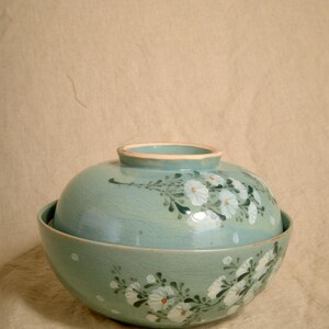 May include: A set of two light blue ceramic bowls with white floral designs. The bowls are stacked on top of each other.