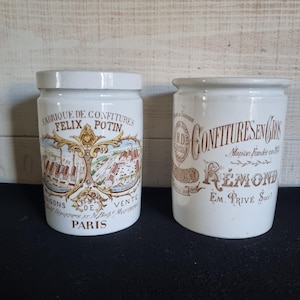 Peut inclure: Deux pots en céramique blanche anciens avec couvercles. L'un porte une illustration et le texte : "FABRIQUE DE CONFITURES FELIX POTIN PARIS". L'autre porte le texte : "CONFITURES EN GROS REMOND".