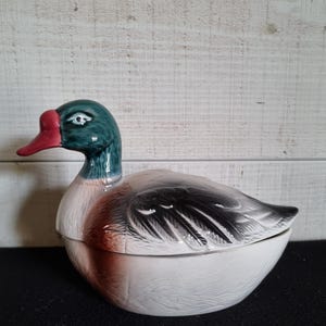 Peut inclure: Un plat en céramique en forme de canard avec un couvercle. Le canard est peint avec des détails réalistes, y compris des plumes vertes, un bec rouge et des marques brunes et noires.