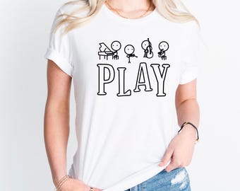May include: White t-shirt featuring a black outline illustration of a piano, violin, cello, and conductor, with the word "PLAY" in bold letters. The design is simple and whimsical, perfect for music lovers.