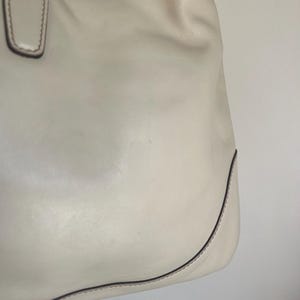 May include: A white leather tote bag with a brown stitch detail around the edges.
