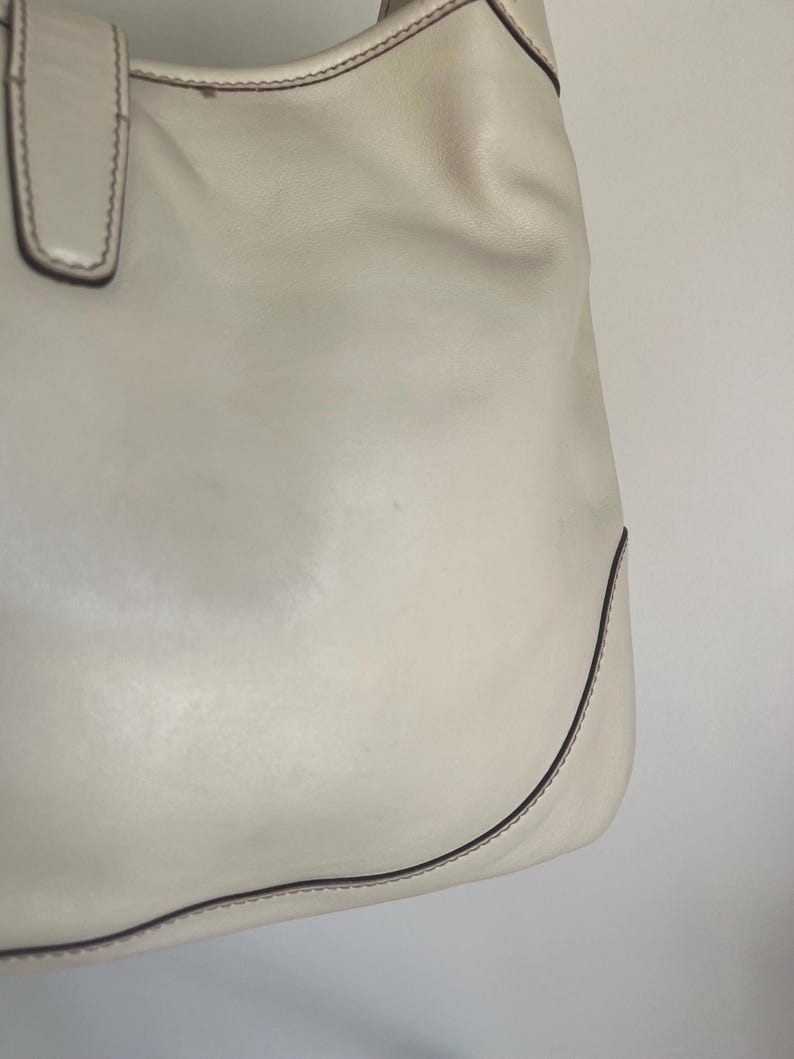 May include: A white leather tote bag with a brown stitch detail around the edges.