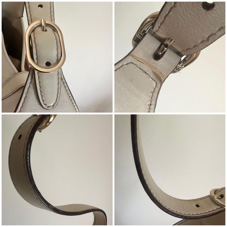 May include: A close-up of a light beige leather handbag with a gold buckle and strap. The bag has a simple, elegant design.