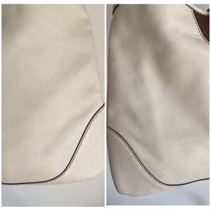 May include: Close-up of the off-white leather of a handbag. The leather has a subtle texture and is stitched with a brown thread.