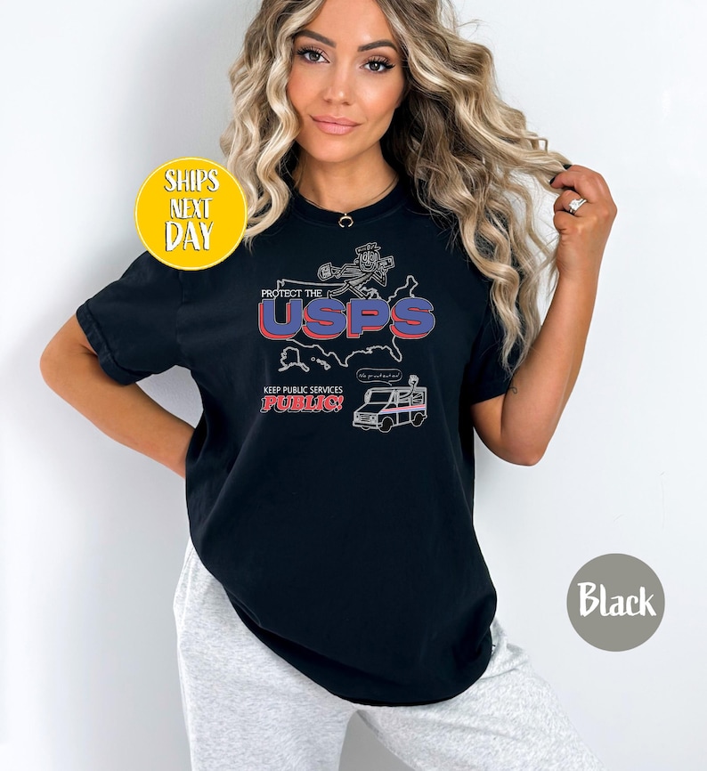 May include: Black t-shirt with a graphic design that reads "Protect the USPS" in red and blue. The design includes a map, a postal worker, and a mail truck. The text "Keep Public Services Public!" is also included.