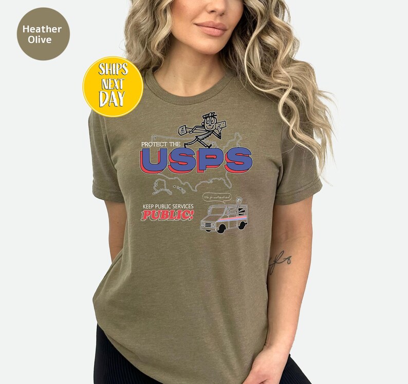 May include: Heather olive-colored t-shirt with a graphic that says "Protect the USPS" in red and blue. The shirt also features a cartoon of a mail carrier and a mail truck. The text "Keep Public Services Public!" is also on the shirt.