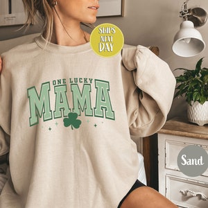 May include: A beige sweatshirt with the text "One Lucky Mama" in green and white lettering with a green shamrock.