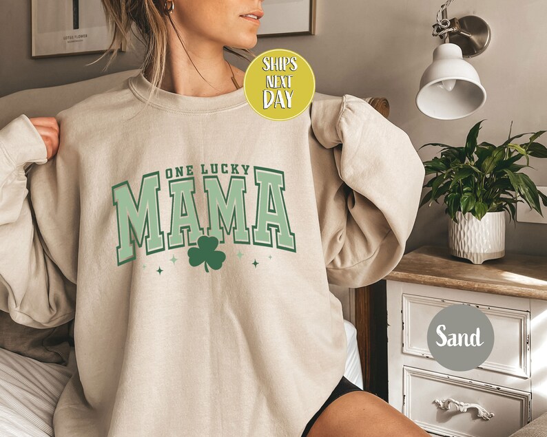 May include: A beige sweatshirt with the text "One Lucky Mama" in green and white lettering with a green shamrock.