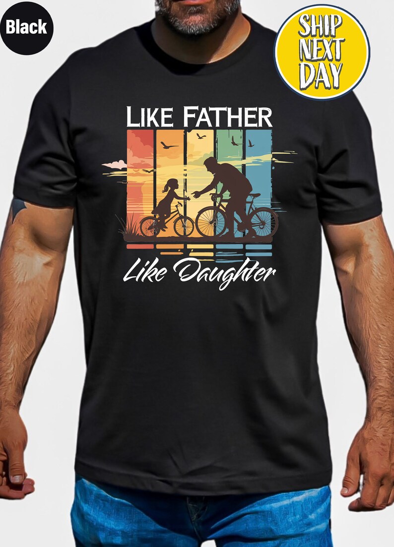 May include: Black t-shirt with a retro-style graphic of a father and daughter riding bicycles. The graphic includes the text "Like Father Like Daughter".