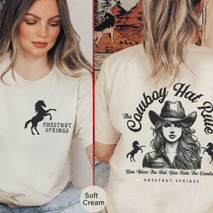 Puede incluir: Una camiseta de color crema con una silueta negra de un caballo y el texto "Chestnut Springs". La parte posterior de la camiseta tiene una ilustración en blanco y negro de una mujer con un sombrero de vaquero con el texto "The Cowboy Hat Rule" y "You Wear The Hat, You Ride The Cowboy" y "Chestnut Springs".