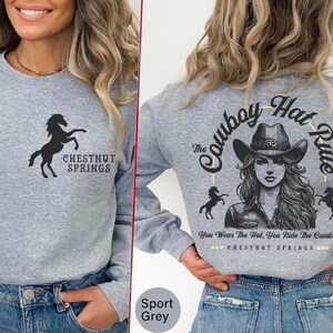 May include: A gray long-sleeve sweatshirt with a black silhouette of a horse and the text "Chestnut Springs" on the front. The back of the sweatshirt features a graphic of a woman wearing a cowboy hat with the text "The Cowboy Hat Rule" and "You Wear The Hat, You Ride The Cowboy" with the text "Chestnut Springs" underneath.