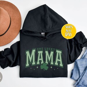 May include: Black hooded sweatshirt with the text "One Lucky Mama" in green with a shamrock graphic.
