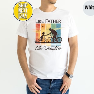 May include: White t-shirt with a vintage-style graphic of a father and daughter riding bicycles. The graphic has a rainbow color scheme and the text "Like Father Like Daughter".