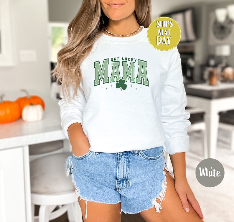 May include: White sweatshirt with a green shamrock and the text "One Lucky Mama" in a green and white varsity style font.