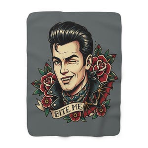 May include: A grey blanket with a vintage-style illustration of a winking vampire with a pompadour hairstyle. The design includes red roses, a bat, and the text "BITE ME" on a banner.