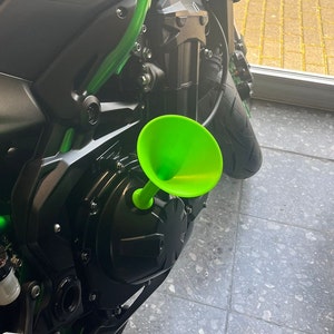 Può includere: Un imbuto di plastica verde attaccato al lato di un motore di moto nero.