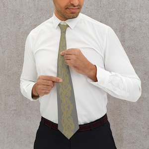 Könnte beinhalten: Eine graue Krawatte mit einem gelben, wellenförmigen, geometrischen Muster. Die Krawatte wird von einer Person getragen, die ein weißes Hemd und eine schwarze Hose trägt. Das Muster der Krawatte ist eine sich wiederholende, abstrakte Linie.