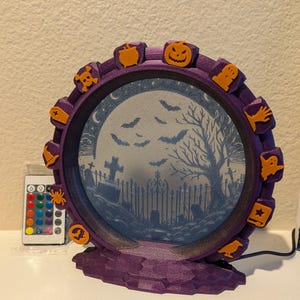 May include: A purple Halloween-themed Ferris wheel decoration with orange accents. The wheel features jack-o'-lanterns, ghosts, and other spooky icons. The center displays a graveyard scene with bats and a full moon. A remote control is included.